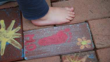 Bunter Fußabdruck auf dem Pflaster neben einem Kinderfuß