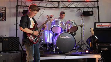 Zwei Jugendliche mit Schlagzeug und Gitarre auf einer Bühne