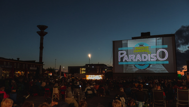 Schaufenster Fischereihafen in der Dämmerung. Viele Menschen sind vor der Leinwand und sehen das Titelbild von "Cinema Paradiso". 
