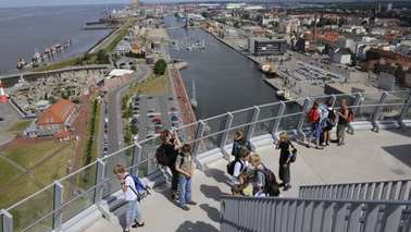 Personen stehen auf einer Aussichtsplattform und schauen auf ein Hafenbecken.