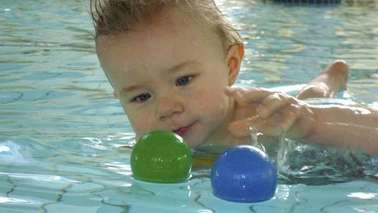 A baby is in the water and playing with balls.