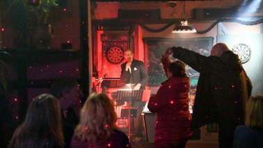 Menschen tanzen, im Hintergrund singt ein Mann neben einem Billiardtisch.