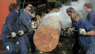 Vir Männer arbeiten an einem Holzmast für ein Segelschiff