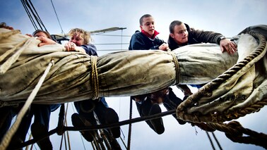 3 junge Menschen raffen die Segel auf einem Schiff