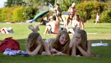  Three young women lie on towels in a meadow.